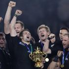 All Black captain Richie McCaw holds the Webb Ellis trophy as teammates celebrate their Rugby...