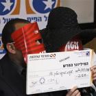 An Israeli couple, wearing masks over their faces to conceal their identity, hold a check for 74...