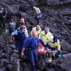 Emergency services negotiate rocks while carrying a teenager to a waiting ambulance after he fell...