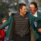 Former champion Phil Mickelson, back, helps Charl Schwartzel of South Africa with his green...