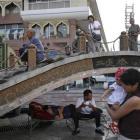 Han Chinese pose for photos on top of a bridge as Uighur men rest underneath, in Urumqi, in China...