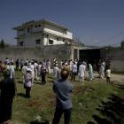 Local people and media gather outside the perimeter wall and sealed gate at the compound and a...