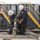 Mody Torres (left) and Josh Anderson connect hoses between a pipeline and water tanks at a Hess...