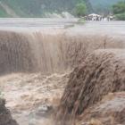 North Koreans stand next to a road as floodwater pours into a caved-in area in Songchon county,...