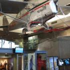 An Auster ZK BDX skiplane hangs above a display of the down bodysuit, ice axe and gloves used by...