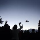 People wave to a Tiger Moth pilot during a flyover at the Lake Hawea Anzac Day dawn service in...