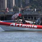 Personnel on a team boat survey damage to the Artemis Racing AC-72 catamaran as it sits in the...