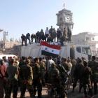 Soldiers loyal to the Syrian regime and civilians gather as they place the Syrian national flag...