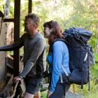 Trampers inspect sawmilling relics and an interpretation board on the Rakiura Great Walk track....