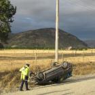 Wanaka constable Bruce McLean with an overturned car on the gravel section of Ballantyne Rd. Mt...