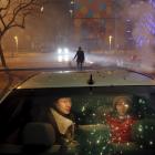 A girl and a woman sit inside the car as firecrackers and fireworks explode celebrating the start...