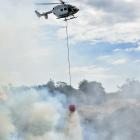 A helicopter douses a grass and gorse fire near Taieri Mouth yesterday. Photo: Gregor Richardson