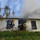 Firefighters get a hose into a burning home in Woodhaugh yesterday, after smashing the glass...