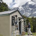 Graeme Stretch and Chris Milne apply their brushes to the Top Forks Hut beneath Mt Pollux, in the...