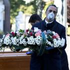 Cemetery workers and funeral agency workers in protective masks transport a coffin of a person...