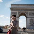A woman wearing a protective mask, walks near Arc de Triomphe as France grapples with an outbreak...