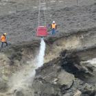 Engineers direct a helicopter monsoon bucket to wash out loosened rock debris from a slip above...