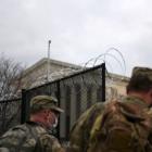 Officers from the National Guard walk near a fence lined with barbed wire at the Capitol grounds...