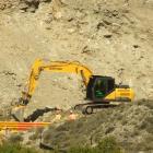 An excavator works to clear debris from the base of the slip that loomed over State Highway 8 in...