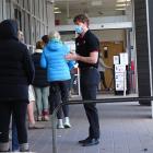 An employee checks shoppers are wearing masks as they line up outside the town centre New World...