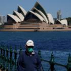 A person in a face mask walks along the harbour waterfront across from the Sydney Opera House....