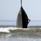 A boat is lifted from the surf by a helicopter after it capsized, forcing its two occupants to...