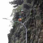 Contractors using abseiling equipment clear loose stones, rock and vegetation from above...