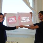 Stencils highlighting migrant challenges are held by Arozo Rafyee (left) and Vaisnavi Nambiar,...