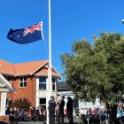 A colour party from HMNZS Toroa raises the Anzac Remembrance New Zealand flag at the commencement...