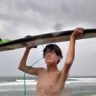 Lenox Gee, 15, of Raglan, shelters under his surfboard at Dunedin’s St Clair Beach as wet weather...