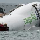 Emergency workers near the cargo plane lying partially in the sea after it veered off the runway...