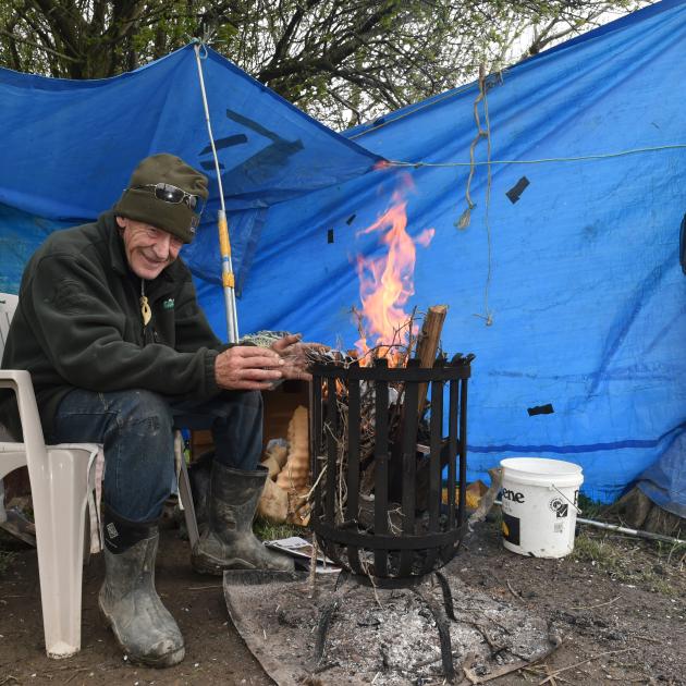 John Carvalho warms his hands at an open fire as wind and rain buffet his whitebait camp near Henley yesterday. Photo: Gregor Richardson