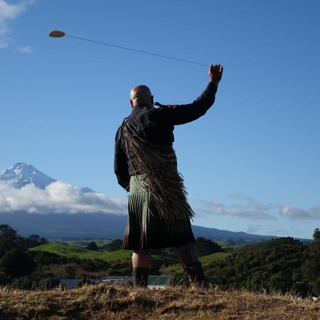 Rangi Kepa swings a purerehua at Parihaka to gather the spirits ahead of the Crown’s arrival for...