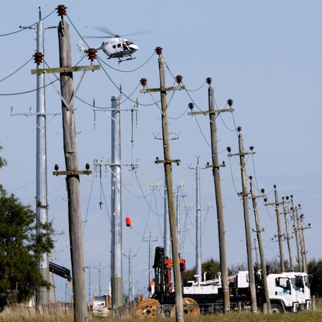 A helicopter positions an electricity line over new poles in Huntly Rd, near Outram, yesterday...