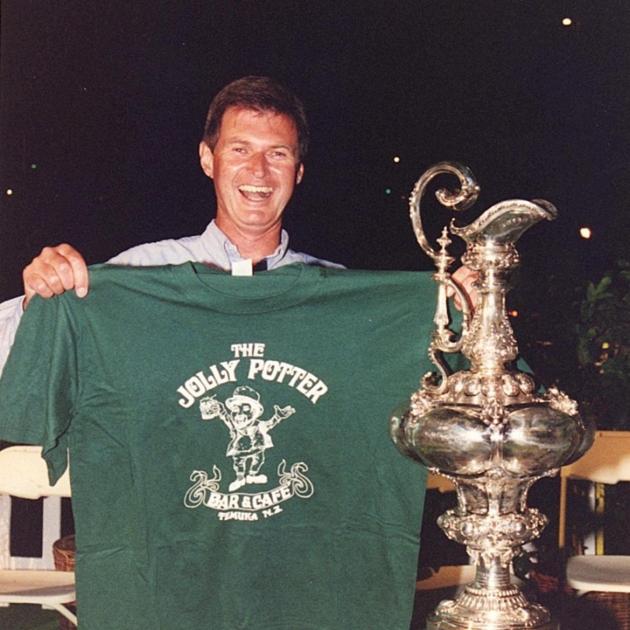 Holding up a Jolly Potter T-shirt, John McBeth celebrates with the Auld Mug aka the America’s Cup.