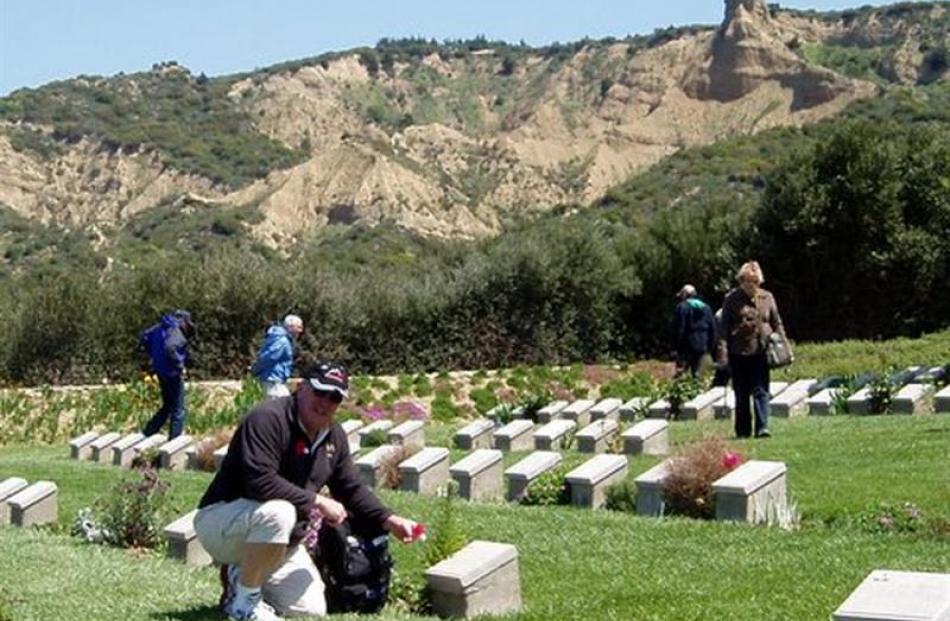 David Geddes places a poppy on a grave at Ari Burnu Cemetery. In the background are the Gallipoli...
