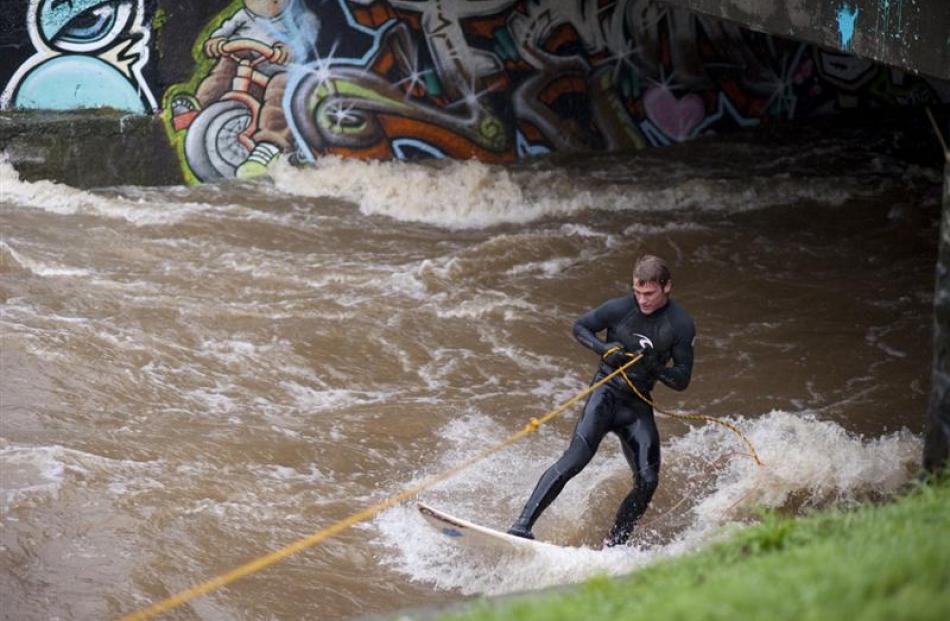 Surfers ride the current on the swollen Leith yesterday afternoon. Photo by Max Bellamy.