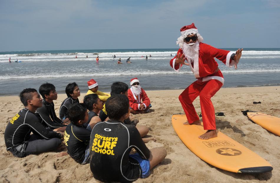 A surfing instructor dressed as Santa gives a lesson to orphans on Kuta Beach in Bali. Photo:...