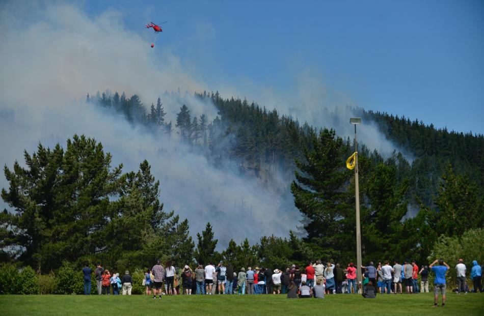 A helicopter with a monsoon bucket fights the fire on Signal Hill, seen flying above a crowd at Opoho Park. Photo: Gerard O'Brien. 