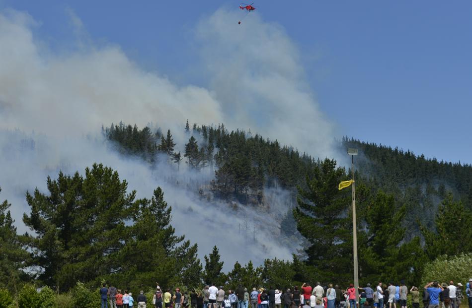 Onlookers at Opoho Park watch as a helicopter with a monsoon bucket operates above the fire on Signal Hill yesterday. Photo by Gerard O'Brien.