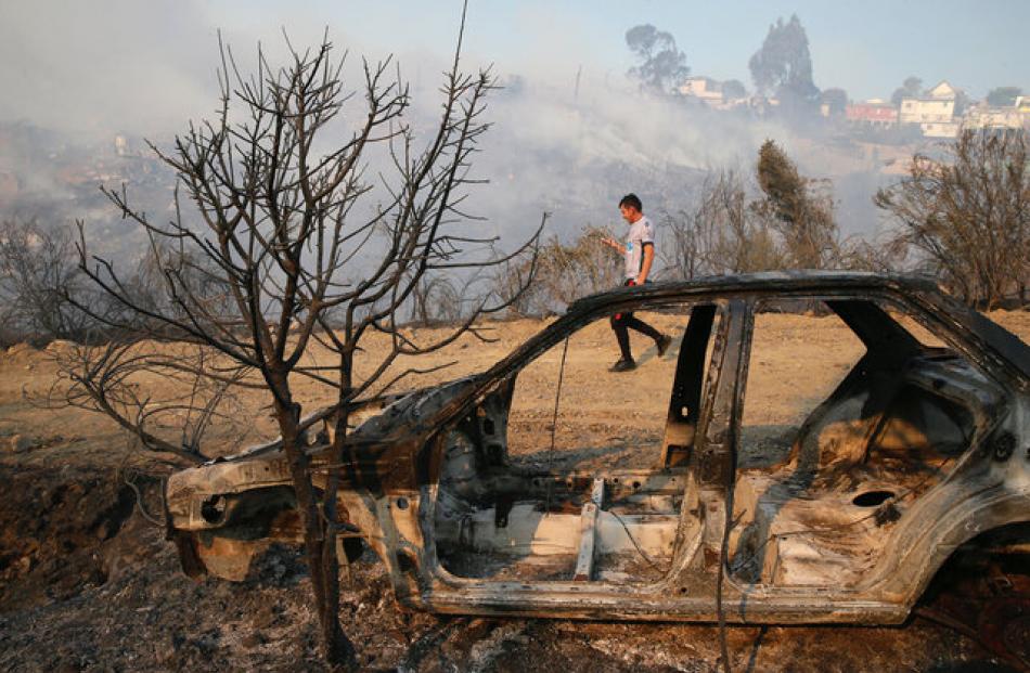 A resident is seen next to a burned car in front of dozens of houses burned on a hill. Photo: Reuters