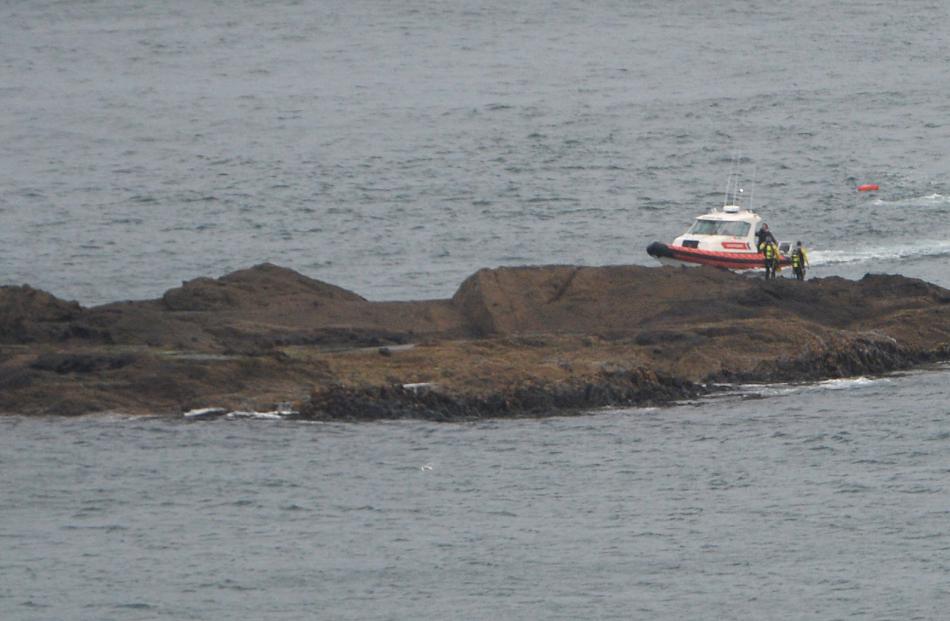 Water rescue personnel stand on a rock off Sandfly Bay near where a diver went missing, as a...