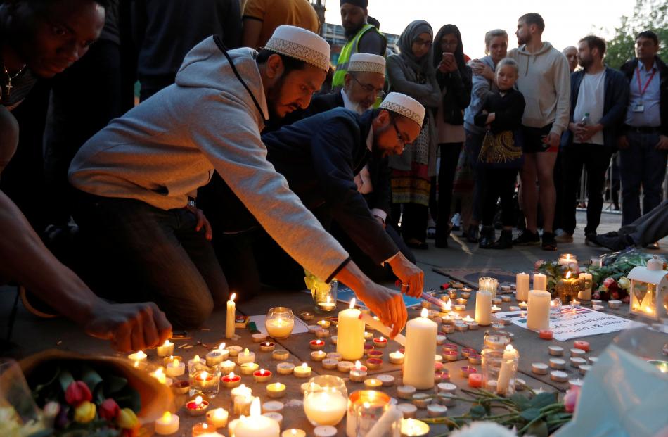 Men light candles following a vigil in central Manchester. Below: Candles and messages of condolence are left for the victims. Photos: Reuters