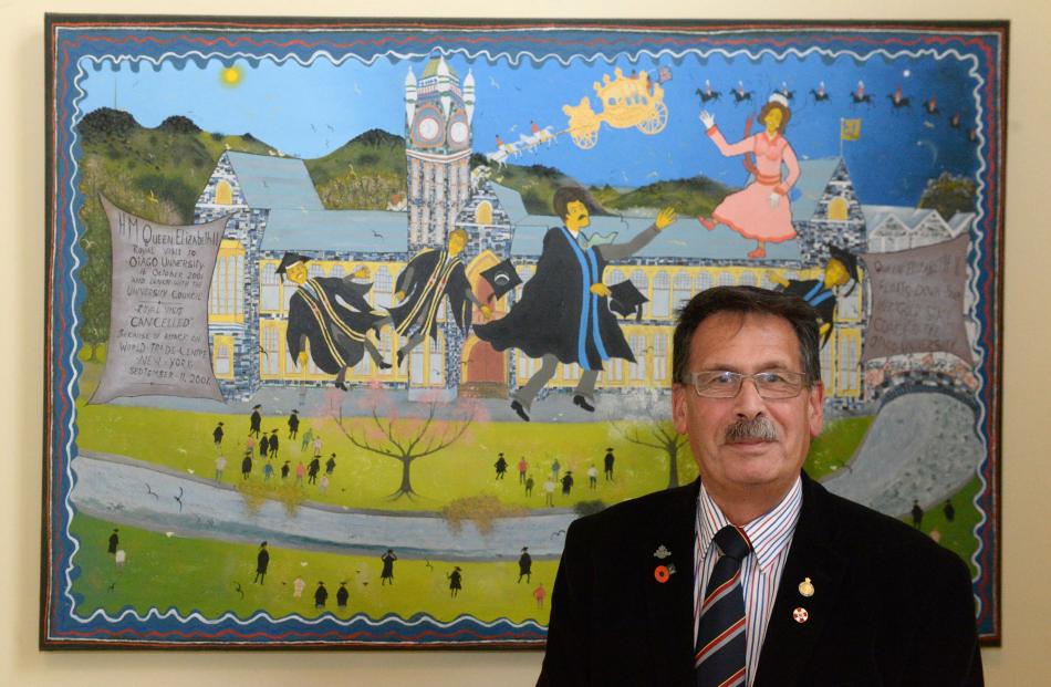 Prof John Broughton, CNZM, stands in front of a painting by Ivan Hill depicting the professor and...