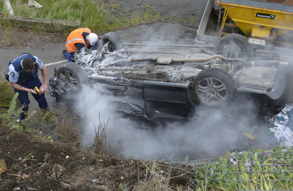 A police officer tries to extinguish a smoking car following a crash on Main South Rd in Green...