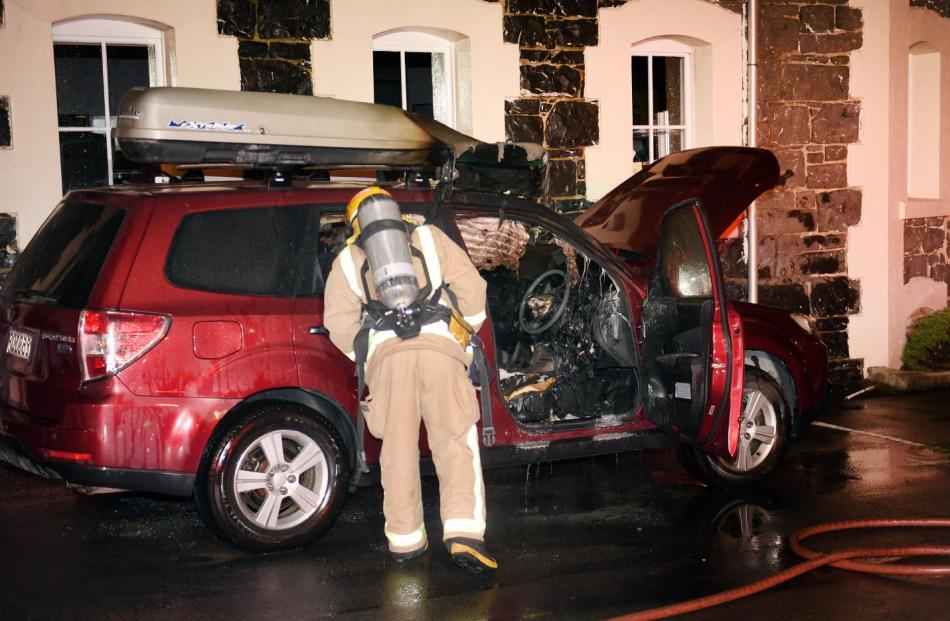 A firefighter inspects a smouldering SUV in North Dunedin in the early hours this morning. Photo:...