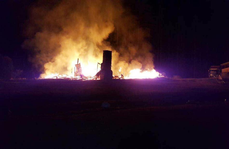 One of the homestead's chimneys is silhouetted in the flames as the house burns. Photo: Anna Williams