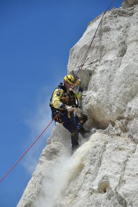 Cromwell firefighter Rowen Dunnet clings to Bowie after abseiling down a cliff (right) to rescue the 2-year-old huntaway at the historic diggings in St Bathans on New Year's Day.