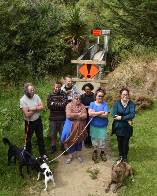 Standing by a flood-damaged and closed suspension footbridge over the Waitati River last week are Waitati residents (front, from left) Gerry Thompson, with Labrador Onyx, Hayden McLean, Louise Booth, Therese Hailes with Jack Russell Tutu, Fleur Sculpher w