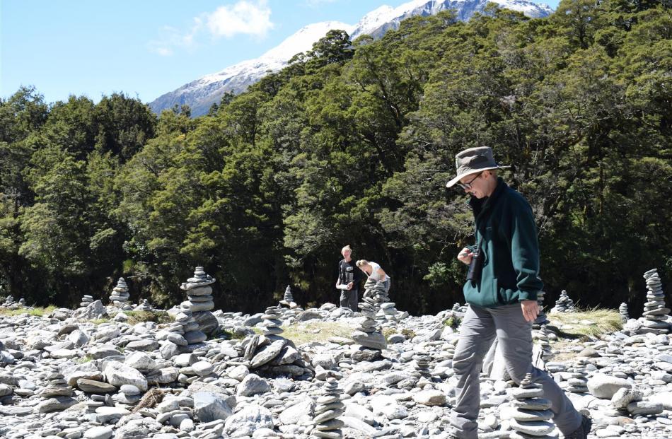 Doc ranger Sophie Briggs walks past Jonatan Johansson and Sara Klint (both 20), of Sweden, trying rock stacking for the first time and adding their stack to the many beside the Blue Pools.